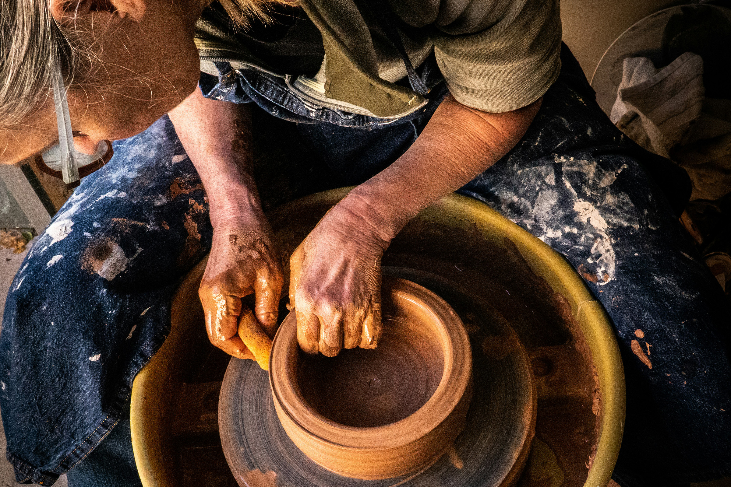 A potter using their hands to sculpt a clay pot on a wheel